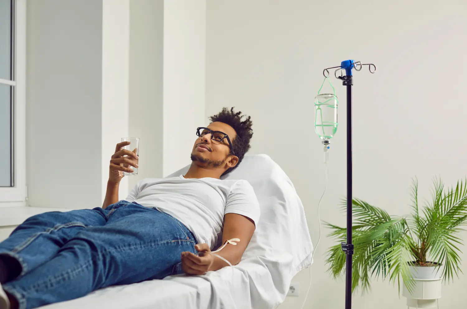 Afroamerikanischer Mann, der in der Klinik oder im Krankenhaus behandelt wird, auf einem medizinischen Bett liegt und eine Medikamenteninfusion erhält